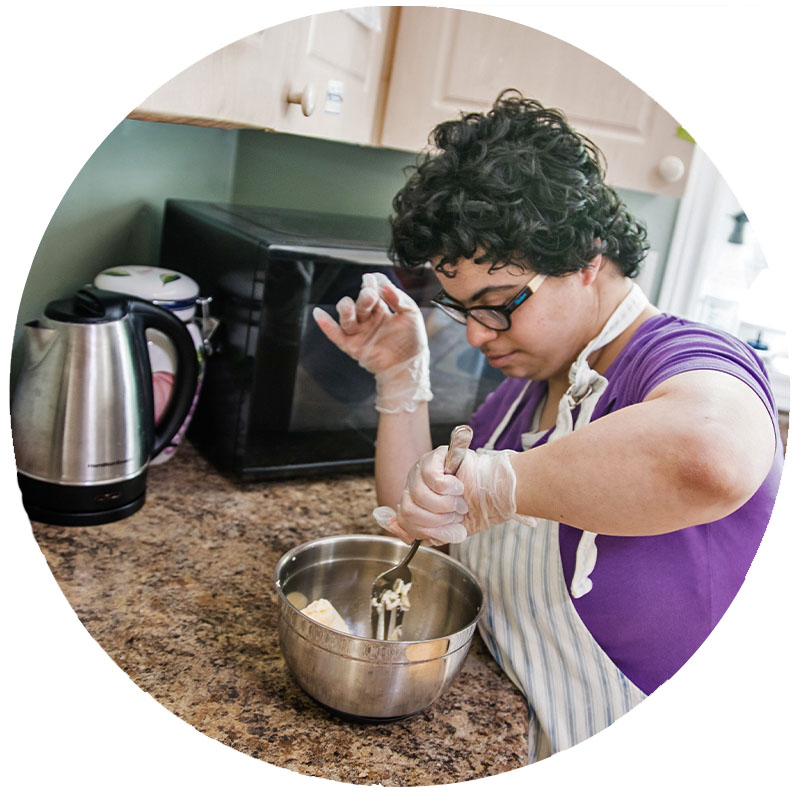 A young woman with Down's Syndrome cooking in the kitchen.