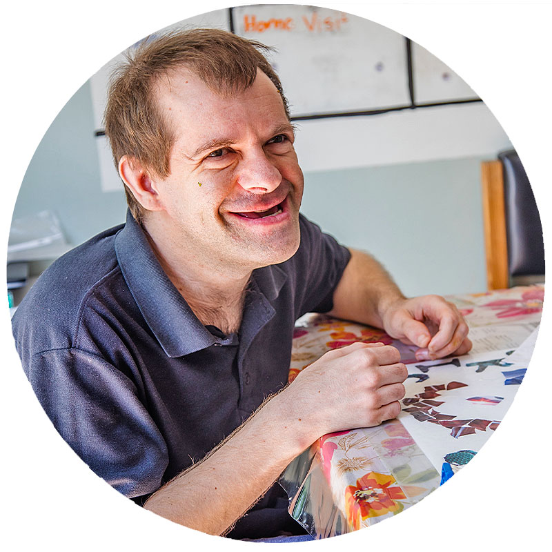 A man with disabilities creating artwork and smiling broadly at the camera.
