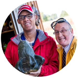 Two adult males with disabilities holding a vegetable from the garden.
